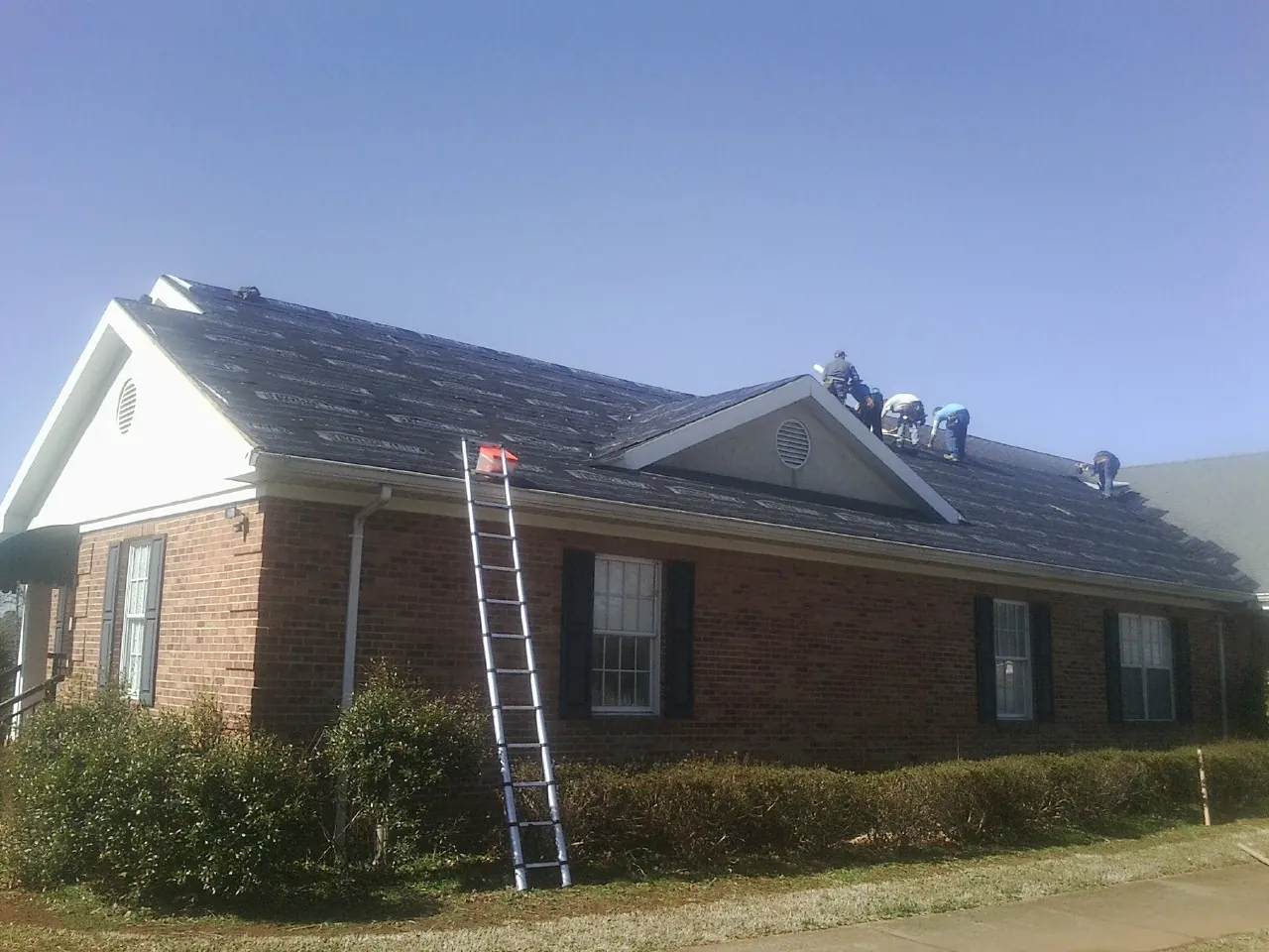 Crew tearing shingles off a brick ranch roof with a ladder set — Emergency Roof Repair work by our crew in Stafford