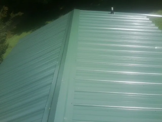 New green metal panels meeting at the ridge of a roof — Flat Roof Repair work by our crew in Stafford
