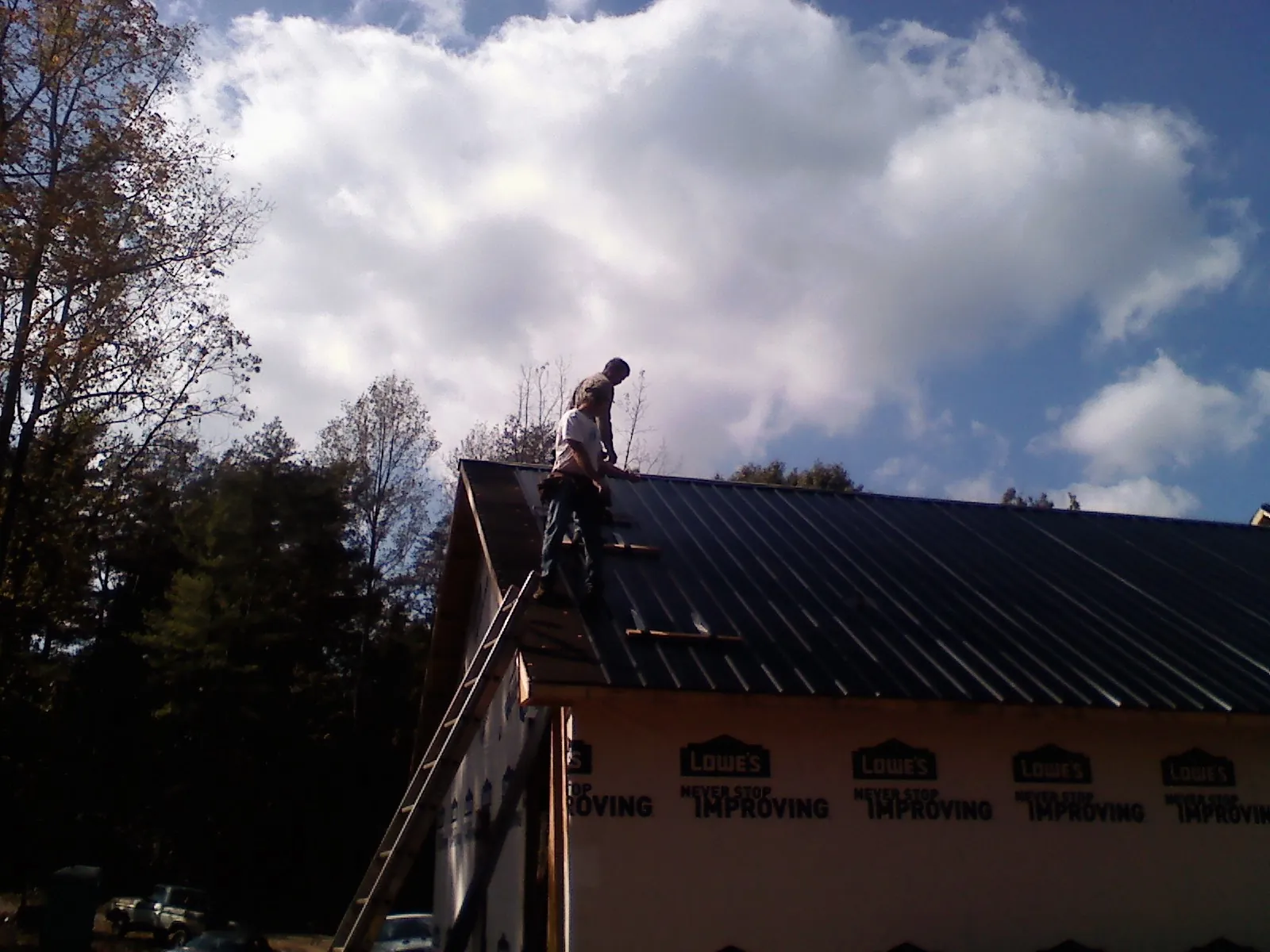 Roofer fastening dark metal panels high against a cloudy sky, from a Roof Inspection job in Stafford