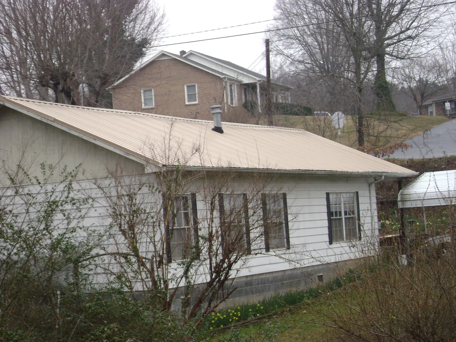 Tan metal roof on a white sided house set into a hillside — Commercial Roofing by Roofing Brothers in Stafford